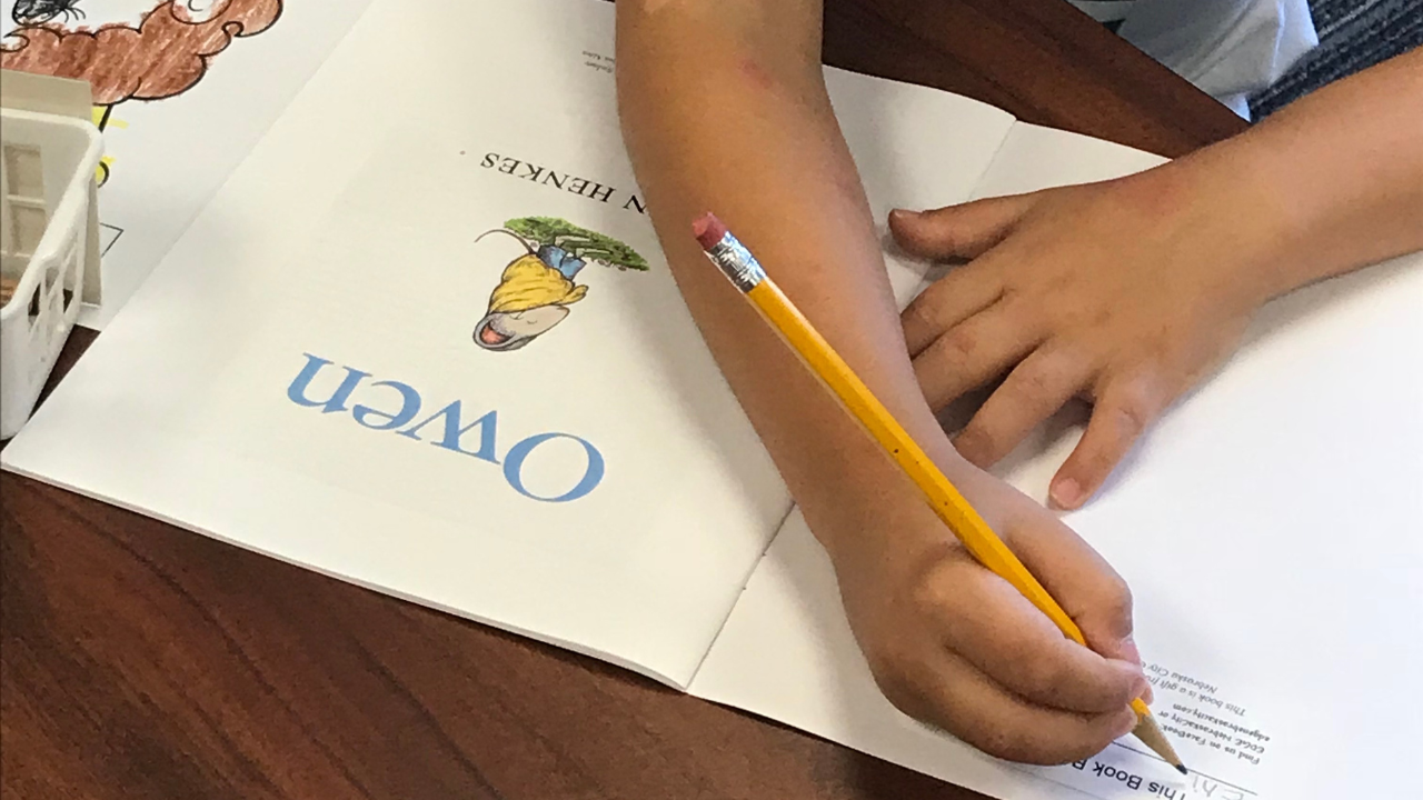 An elementary schooler writes his name in his personal copy of the children’s book.