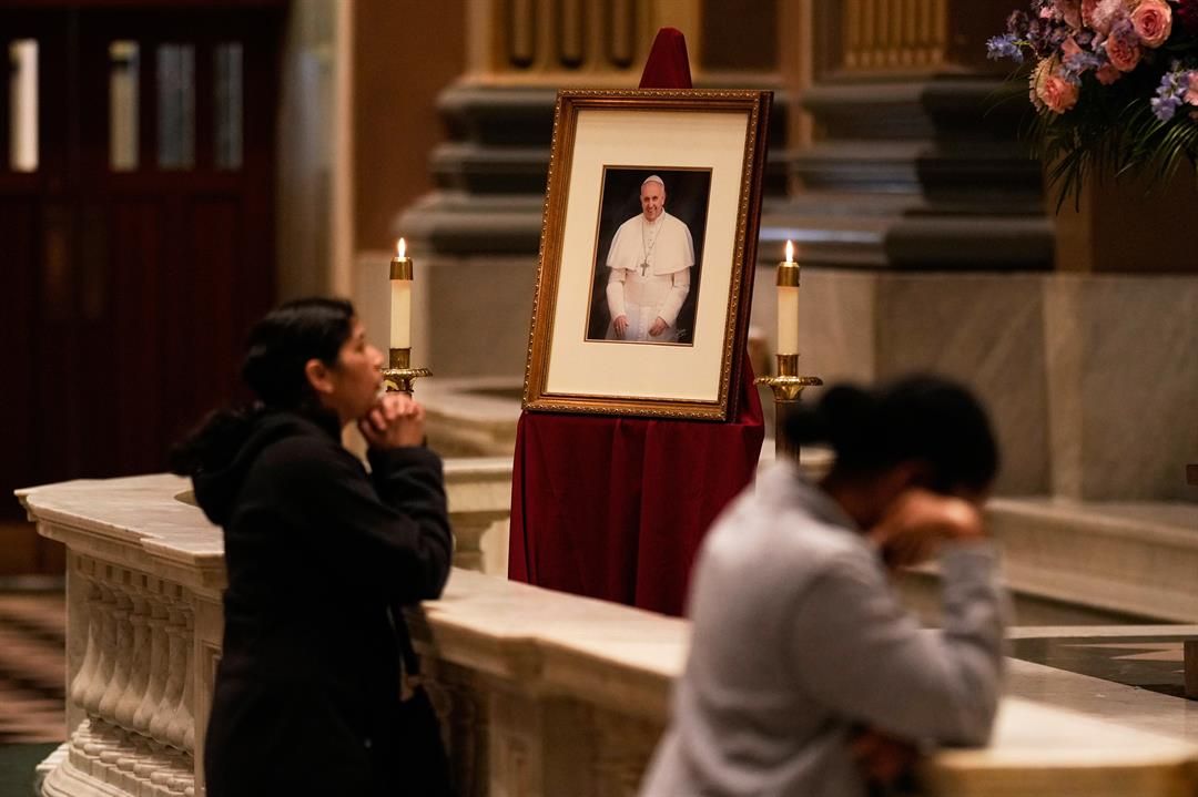 People pray near a picture of Pope Francis inside the Cathedral Basilica of Saints Peter and Paul, Monday, April 21, 2025, in Philadelphia. (AP Photo/Matt Slocum)